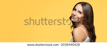 Portrait photo of smiling lovely woman in white casual clothing, posing over yellow color background. Brunette girl posing at studio. Wide composition with copy space free area for text. Female model.