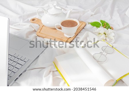 Modern home office desk with laptop, book, tea latte cup on messy bed background. Flat lay, top view. Autumn, fall concept.