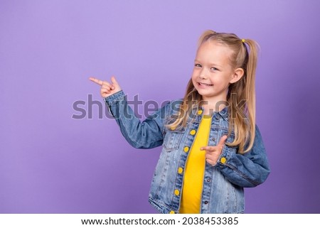 Photo of young little girl happy positive smile point fingers empty space ads promo choose isolated over violet color background