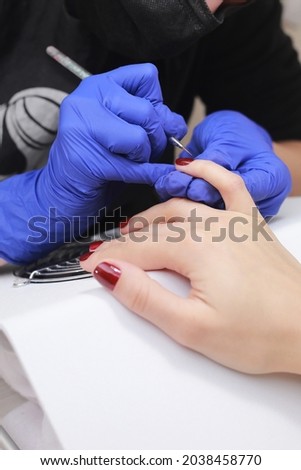 Master in protective mask and gloves during a manicure at beauty salon. Master manicurist varnishes the marsala gel on the nails of a female client. The concept of beauty and health
