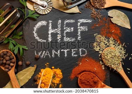 Chef wanted written on black stone tile with white chalk, surrounded by condiments an kitchen tools (paprika, curcuma, all spice, parsley, wood spoons Royalty-Free Stock Photo #2038470815