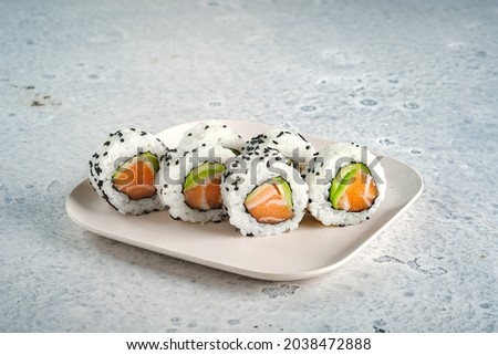 A set of fresh sushi rolls with salmon, avocado and black sesame seeds served on a plate. Japanese sushi uramaki or California roll