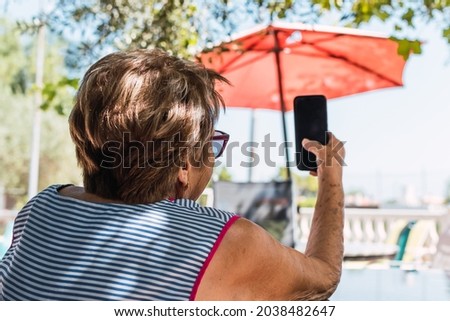 old woman taking a selfie on a sunny day under an umbrella