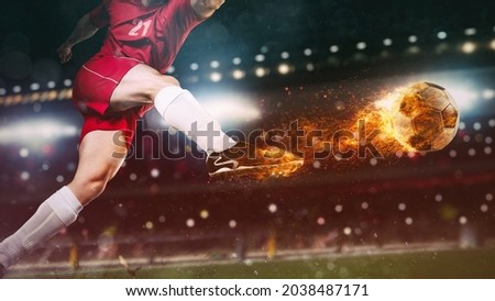 Close up of a soccer scene at night match with player in a red uniform kicking a fiery ball with power Royalty-Free Stock Photo #2038487171