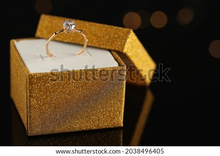 Beautiful engagement ring in box against blurred festive lights, space for text