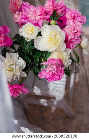 a bouquet of fresh white and pink peonies in a transparent glass vase with beautiful shadows near a white curtain tulle, in blur.