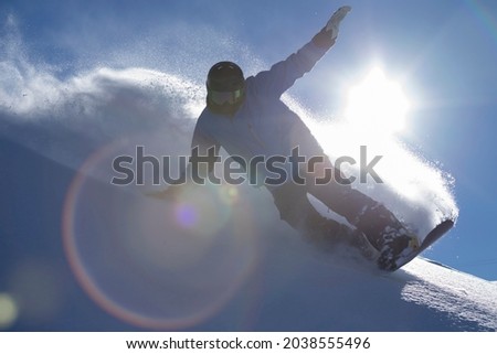 Having fun on a snowboard and feeling free. Fresh powder, no friends on a powder day. The sky is blue and the light gets into the lens forming a flare. Light snow and speed. , Copy space