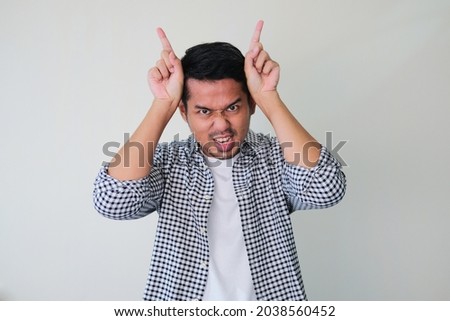 Adult Asian man showing angry face expression and making evil horn using his fingers