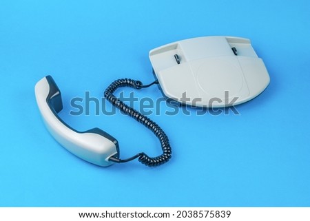 A gray phone with the receiver off on a blue background. Retro means of communication.