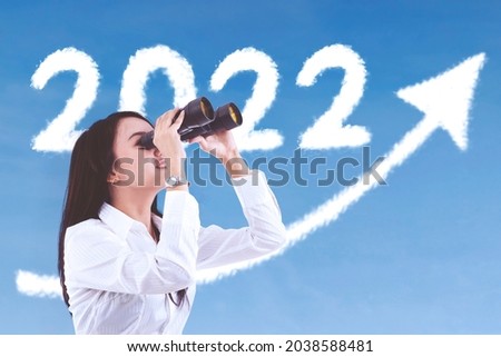 Female entrepreneur using binoculars while looking at clouds shaped 2022 numbers and upward arrow in the sky