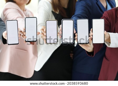 Businesspeople sitting together in office over working desk with colorful graph and charts pater, hold smartphones in different model with blank screens.