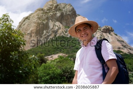 Smiling latin tourist with hat and backpack, on a mountain. Smiling man in Peña de Bernal traveling. Vacation concept