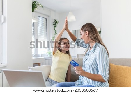 Low angle of excited small daughter giving high five to mother and screaming while celebrating successful online shopping using laptop at table in light living room