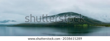 A Misty Lake With Rolling Fog Against a Green Mountain Background Royalty-Free Stock Photo #2038615289