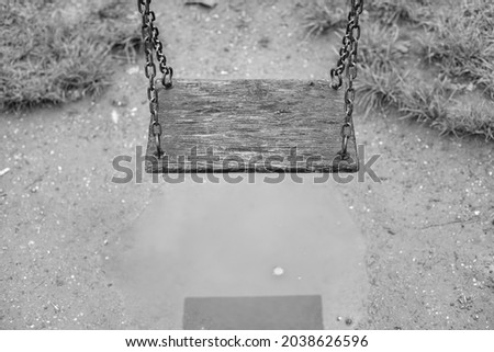 Close up of a children's wooden swing on chains above the pond after the rain. Black and white photograph.