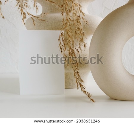 Blank paper mockup and modern beige vasen with dry grass on white desk with copy space.
Card Mockup,branding.
