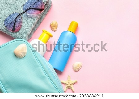 Bag with sunscreen cream, towel and sunglasses on color background