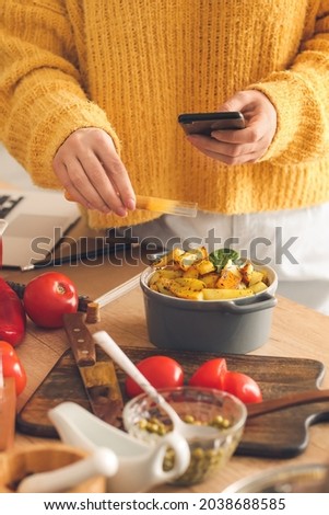 Female food photographer with mobile phone taking picture of tasty potatoes in kitchen