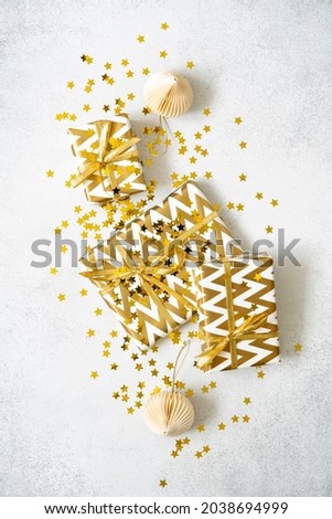 Christmas gifts, star confetti and decorations on grey textured background. Birthday presents wrapped in golden paper with geometric print. Celebration concept. New year composition.