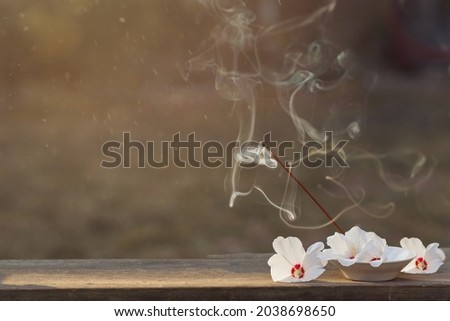 Incense sticks with incense smoke and beautiful white flowers in a bowl on a wooden table. Banner for design and advertising of spiritual practices. The concept of peace and inner balance. Copyspace