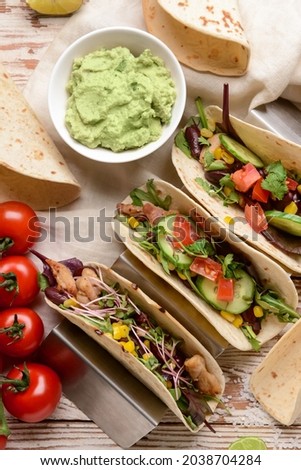 Composition with tacos and tasty guacamole in bowl on light wooden background