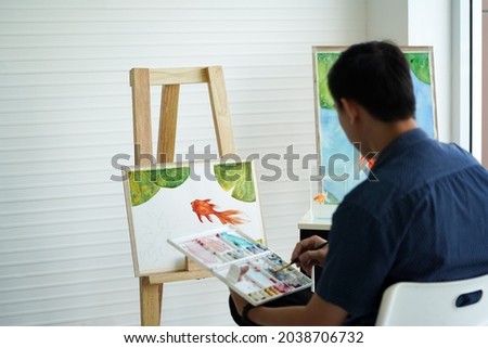 Young asian man drawing a goldfish and lotus leaf on white board in watercolor painting art classes