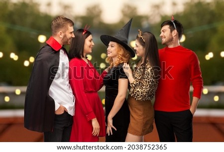 friendship, holiday and people concept - group of happy smiling friends in halloween costumes of vampire, devil, witch and cheetah over roof top party background