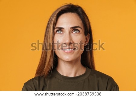 European ginger woman in t-shirt smiling while looking upward isolated over yellow background