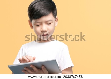 Kids and internet technology concept. Portrait or a smart look asian little boy enjoy using touch screen device to remote learning from home during Covid 19 pandemic. Screen time, Watching cartoon.