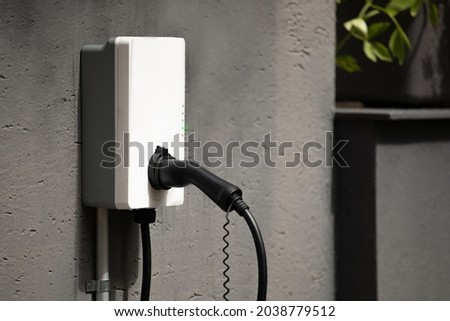 plug holder for wall mount charging station with cable at wall box mounted to concrete house wall ready to load and tank electrical cars with power instead of gasoline to be an alternative way of fuel Royalty-Free Stock Photo #2038779512