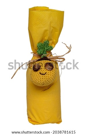 Gift packaging isolated. Closeup of a bottle wrapped with a yellow napkin and tied with a homemade funny face made of fabric and buttons as a pendant. Macro.