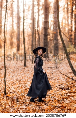 witch in the autumn forest. A girl in a black long dress walks in the forest.