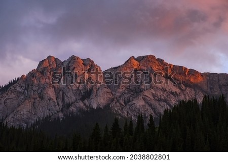 Beautiful pink sunset in rocky mountains with pink clouds on background. Nature landscape background. Wilderness background. Komirshi gorge in Kazakhstan. Travel journey concept.
