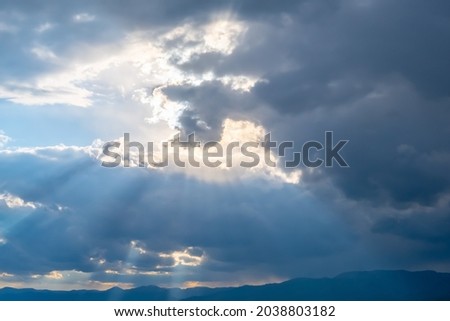 Cloudy blue sky with sunrays shining though them. Dramatic cloudscape.