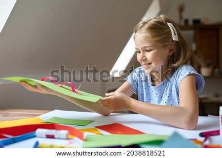 Female child glues colored paper at the table