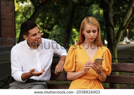 Young woman with smartphone ignoring her boyfriend in park. Boring date Royalty-Free Stock Photo #2038826003