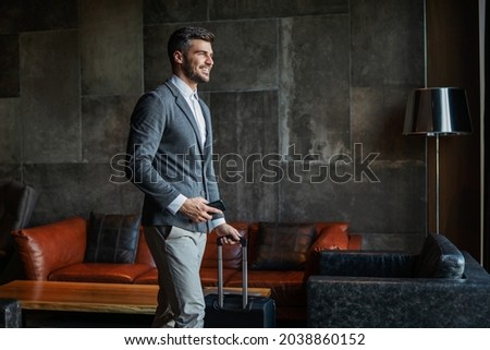 A male businessman dressed elegantly carries luggage and a mobile phone in the hotel lobby. He's on a business trip. Travel, symposium, ready to go Royalty-Free Stock Photo #2038860152