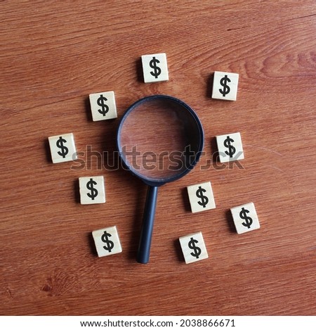 Magnifying glass surrounded by wooden cubes with dollar icon. Looking for money, looking for cash concept