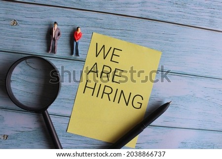 Top view of miniature people and magnifying glass with text WE ARE HIRING