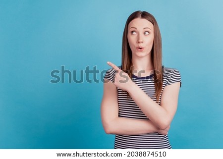 Portrait of excited curious girl indicate finger empty space on blue background