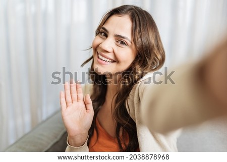Beautiful young Latin smiling face woman holding camera or phone in hand and she makes video call or she is recording video for her fans, video call and vlogger concept POV Royalty-Free Stock Photo #2038878968