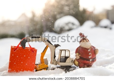 Two models of toy excavators, a souvenir Santa Claus, a gift bag stand in snow. concept for Christmas business greetings, New Year holidays in construction companies. Sunny winter holiday