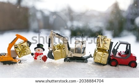 Two models of toy excavators, red forklift, souvenir snowman, gifts in gold paper stand in a row in snow. Creative congratulation construction companies merry christmas, new year winter holidays