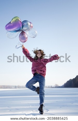 graceful slender cute teenage girl, holding many colorful balloons in her hands, jumping up on the snowy ground. winter holidays. Joyful emotions, vitality, no problems. fun, surprise, joy