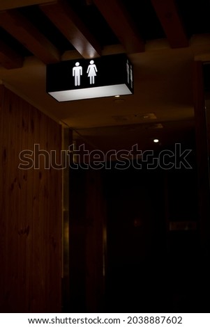Rest room sign hanged on the ceiling in a dark corner of Chinese restaurant with wooden wall and cozy interior.