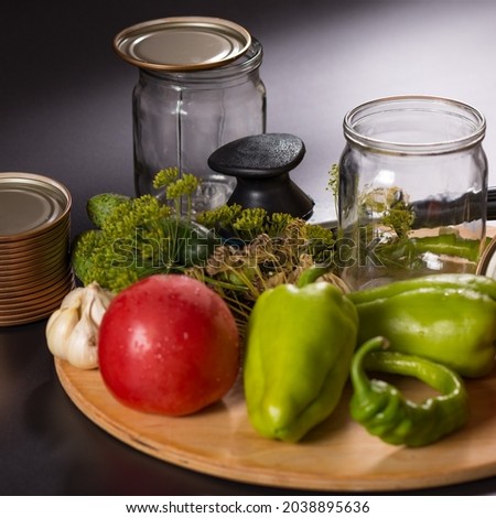 Canning vegetables in glass jars with canning tool on wooden board, on black background.