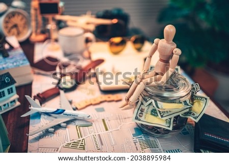 Wood human doll sitting on Saving money in glass jar for travel, holiday, vocation on road map on the table. Travel budget concept. 
