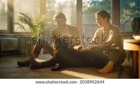 At Home: Happy Couple Play with Their Dog, Gorgeous Brown Labrador Retriever. Boyfriend and Girlfriend Tease, Pet and Scratch Super Happy Doggy, Have Fun in the Stylish Living Room Royalty-Free Stock Photo #2038902644