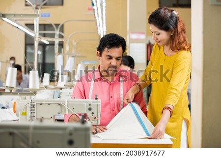 Female guiding male textile worker marking on garment at factory Royalty-Free Stock Photo #2038917677