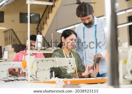 Male instructor explaining female textile worker by using mobile phone at factory